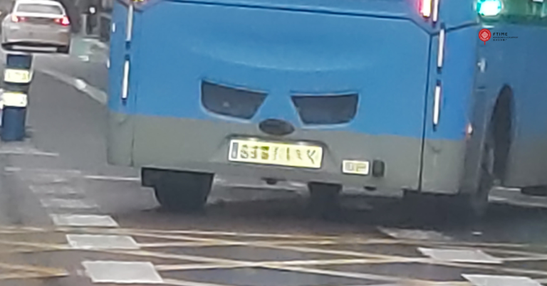 Parte trasera de un autobús azul circulando por una calle de Madrid a media tarde. La disposición de las luces y rejillas traseras crea la apariencia de una cara enfadada, con cejas fruncidas y una expresión seria, mientras el autobús gira a la derecha en un cruce urbano.