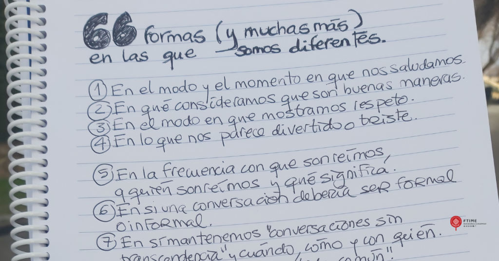 otografía de un cuaderno de espiral abierto, con hojas de líneas y texto escrito a mano en tinta negra. En la parte superior se lee el título “66 formas (y muchas más) en las que somos diferentes”. Debajo aparece una lista numerada con ejemplos de diferencias culturales relacionadas con la comunicación, el trato, el tiempo y la toma de decisiones. El cuaderno está sostenido al aire libre, con un fondo desenfocado.